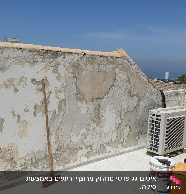 קיר מתקלף עם דלי צבע ומטאטא על הגג